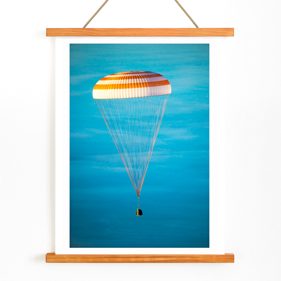 Soyuz TMA-14M spacecraft descending with parachute against blue sky NASA Expedition 42 landing poster artwork, with wooden magnetic frame on white background