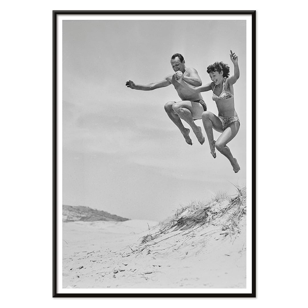 Two Tivoli Stars performing an acrobatic jump on a sandy beach in swimsuits Acrobatics at the Beach poster, with black aluminium frame on white background