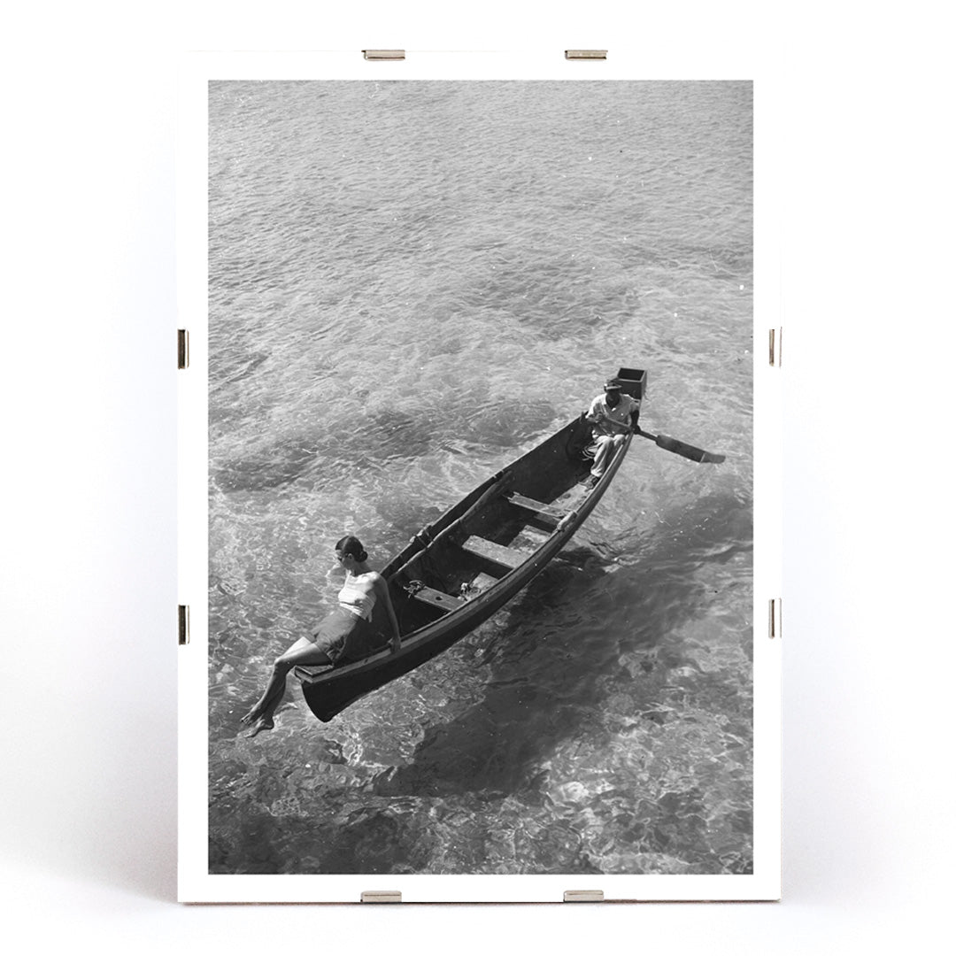 Fashion model on boat edge with man rowing in clear water Montego Bay Jamaica by Toni Frissell artwork poster, framed and displayed in modern living room decor