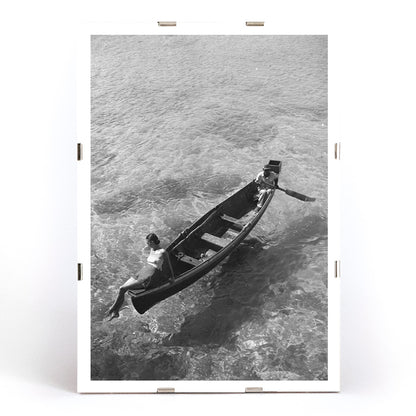 Fashion model on boat edge with man rowing in clear water Montego Bay Jamaica by Toni Frissell artwork poster, framed and displayed in modern living room decor