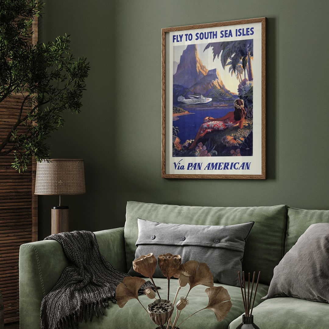 Vintage travel poster of a woman in a floral dress on a tropical island with a Pan American seaplane by Paul George Lawler, framed and displayed in home decor