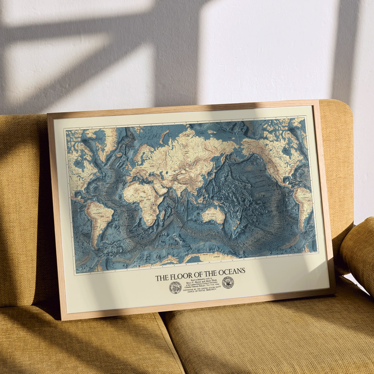 World map artwork showing ocean floors titled The Floor of the Oceans bathymetric map poster, framed and displayed in modern living room decor