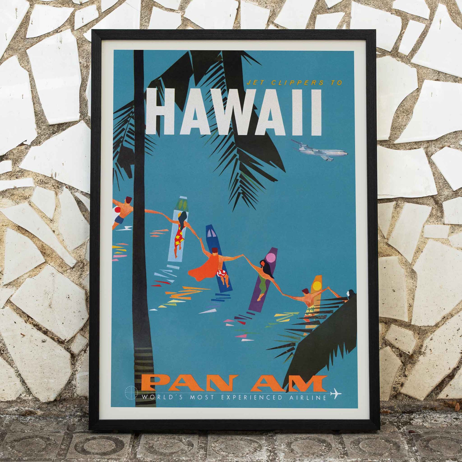 Colorful travel poster Jet Clipper to Hawaii by Pan Am Airlines with palm trees surfers dancers on surfboards and airplane above palm leaves, framed and displayed in home decor