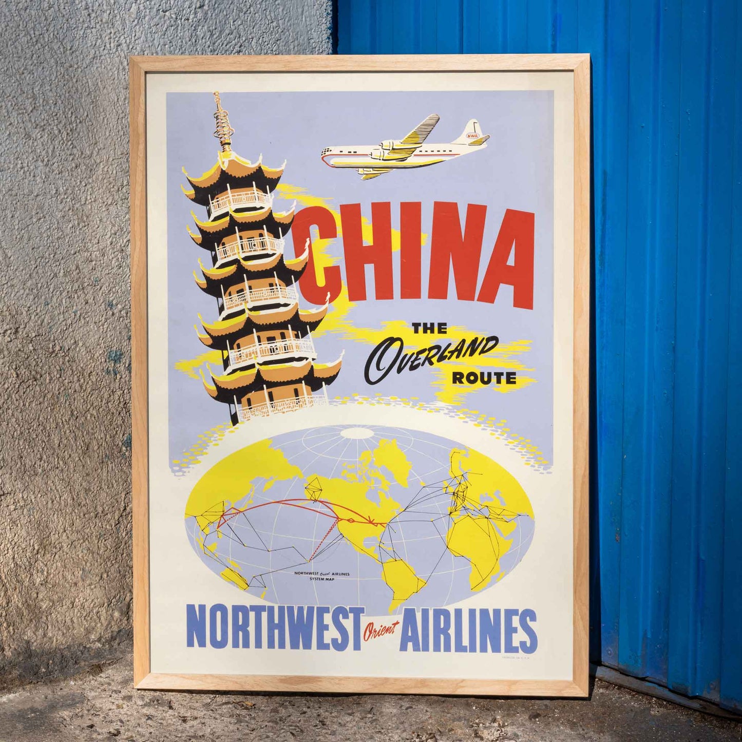 Vintage travel poster of China featuring a pagoda airplane and world map promoting the overland route by Northwest Orient Airlines, framed and displayed in home decor