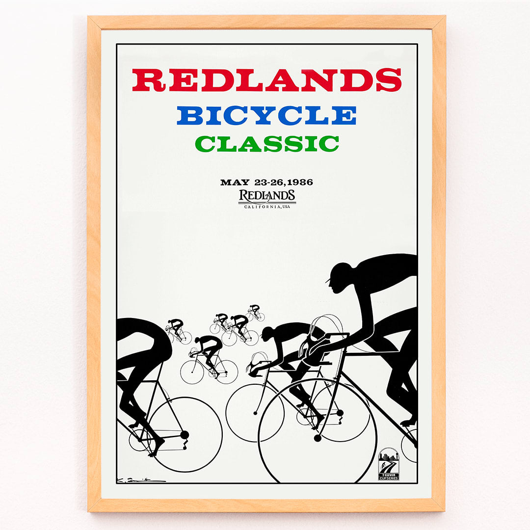 Cyclists racing illustration and poster by Karlis Smiltens titled Redlands Bicycle Classic featuring red blue and green text on white background, framed and displayed in modern living room decor